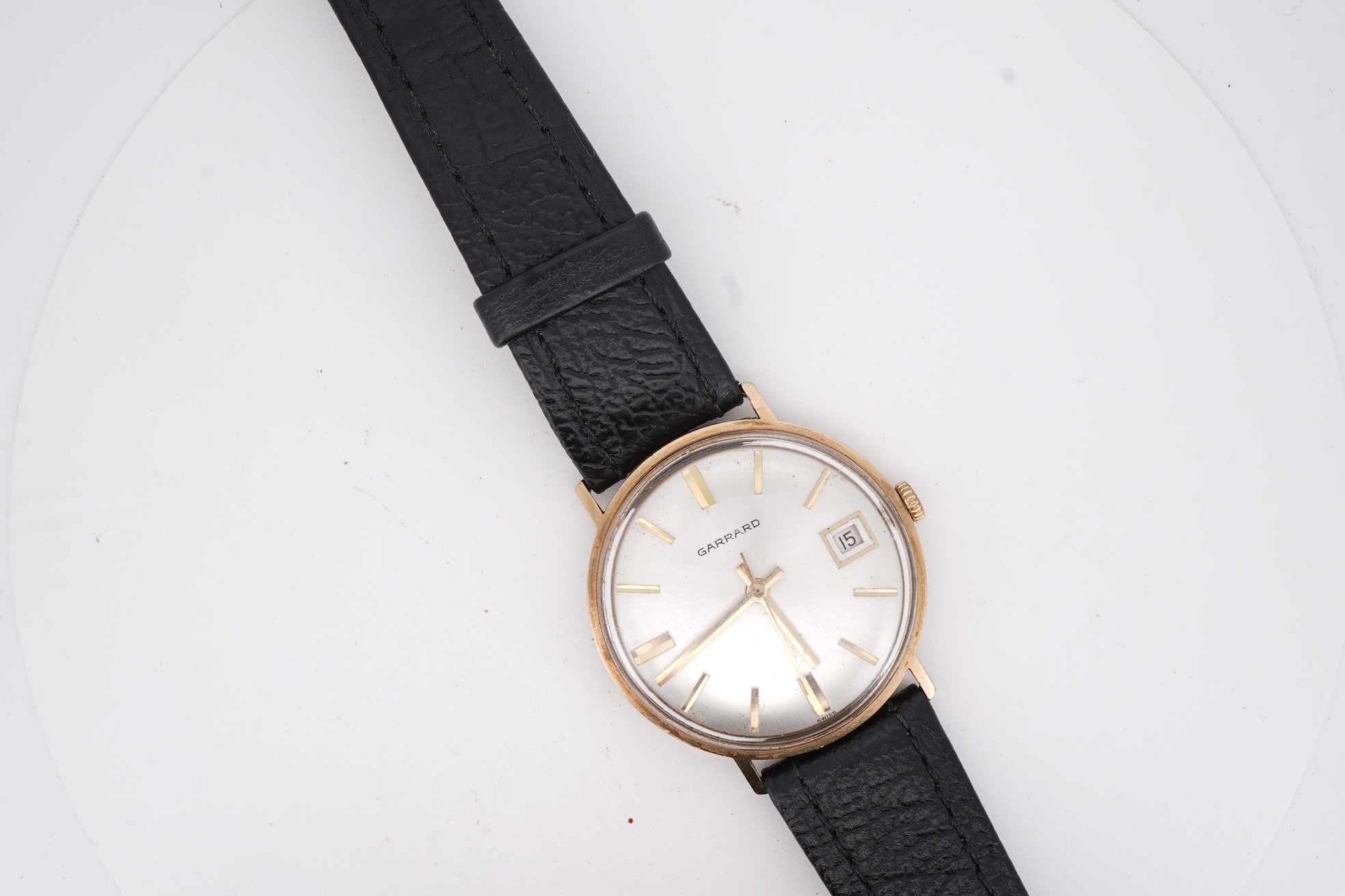 A gentleman's yellow metal Garrard manual wind wrist watch, with baton numerals and date aperture, case diameter 34mm, on a black leather strap.
